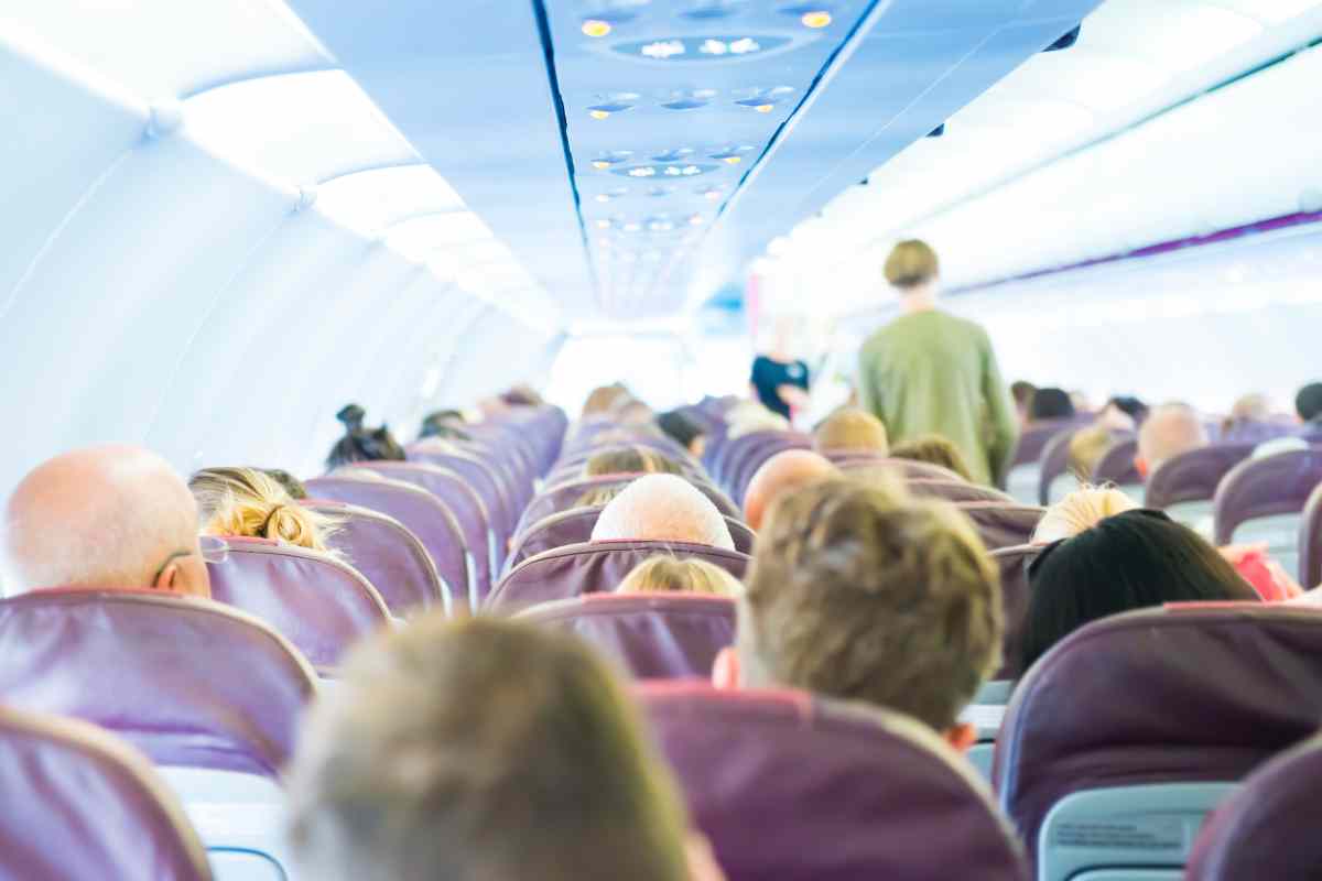 cabina di un aereo piena di passeggeri e uno è in piedi