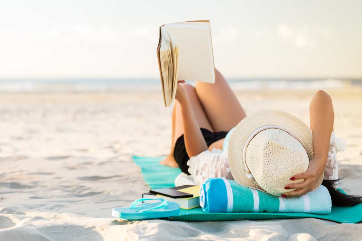 donna sdraiata in spiaggia che legge un libro