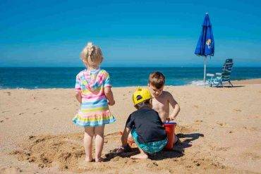 tre bambini giocano in spiaggia ombrellone sedia