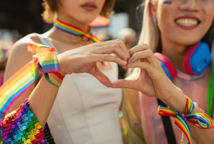 coppia di ragazze con bandiere LGBT che fa il segno del cuore con la mano